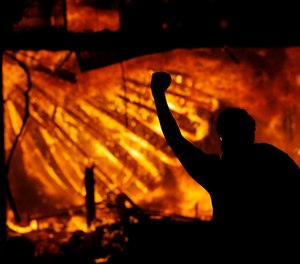 A protester gestures in front of the burning 3rd Precinct building of the Minneapolis Police Department on Thursday, May 28, 2020, in Minneapolis.