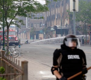 A firefighter directs water on a burned building as one of the state troopers patrols the area Friday, May 29, 2020 after another night of protests over the death of George Floyd who died in police custody Monday in Minneapolis. (AP Photo/Jim Mone)