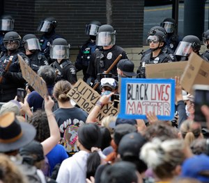 Police officers behind a barricade watch as protesters fill the street in front of Seattle City Hall on Wednesday, June 3, 2020, in Seattle. Seattle City Councilmember Andrew Lewis has introduced legislation that would divert police funds to a program that would dispatch medics and crisis workers to mental health calls.