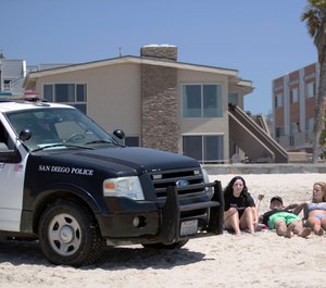 In this May 22, 2020, file photo, San Diego police officers ask three people to get up from the beach, which was closed to sitting or lying down, in San Diego. (AP Photo/Gregory Bull, File)