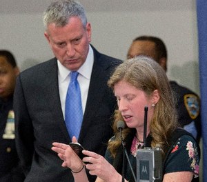 New York City Mayor Bill de Blasio, left, joins NYPD Deputy Commissioner of Information Technology Jessica Tisch as she uses a smart phone to gather information to answer a reporters question during a news conference, Tuesday, Feb. 23, 2016, at police headquarters in New York.