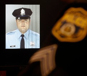 An officer sits next to a displayed image of Officer Jesse Hartnett ahead of a news conference Friday, Jan. 8, 2016, in Philadelphia. (AP Photo/Matt Rourke)