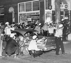 Cleveland police and newsmen take cover in the Hungarian neighborhood of Cleveland, OH, where a sniper was suspected of shooting from the roof tops on July 23, 1966.