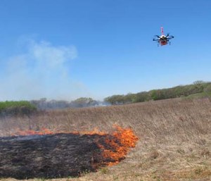 A drone designed to ignite controlled grass fires comes in for a landing in a field.