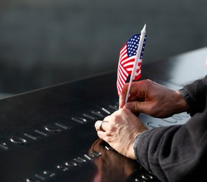 A man adjusts a flag that was inserted in the name of one of the New York City Police Department's first responders at the South Pool of the National September 11 Memorial & Museum, Monday, Nov. 9, 2015, in New York, following a ceremony honoring 9/11 first responders who were also military veterans.
