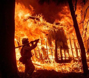 Firefighter Jose Corona sprays water as flames consume from the Camp Fire consume a home in Magalia, Calif., on Friday, Nov. 9, 2018.