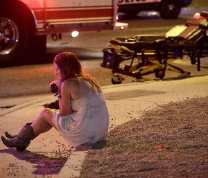 A woman sits on a curb at the scene of a shooting outside of a music festival along the Las Vegas Strip, Monday, Oct. 2, 2017, in Las Vegas. Multiple victims were being transported to hospitals after a shooting late Sunday at a music festival on the Las Vegas Strip.