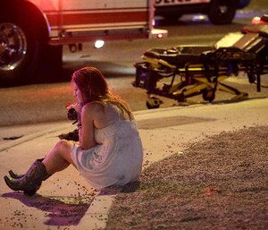 A woman sits on a curb at the scene of a shooting outside of a music festival along the Las Vegas Strip, Monday, Oct. 2, 2017, in Las Vegas. Multiple victims were being transported to hospitals after a shooting late Sunday at a music festival on the Las Vegas Strip.