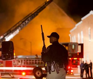 An officer stands near a blaze, April 27, after rioters plunged part of Baltimore into chaos, torching a pharmacy, setting police cars ablaze and throwing bricks at officers. (AP Photo/Matt Rourke)