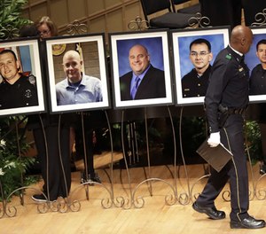 In this July 12 2016 file photo, a member of the Dallas Police Choir passes the portraits of five fallen officers prior to a memorial service in Dallas. More than a dozen states this year have passed “Blue Lives Matter” laws that come down even harder on crimes against law enforcement officers. The new laws came in reaction to a spike in deadly attacks on police last year.
