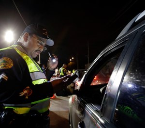 In this Thursday, Jan. 29, 2015 photo, Miami police officer Luis Ortiz looks at a driver's license he requested from a motorist during a drunk-driving checkpoint in Miami.