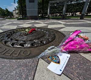 In this July 8, 2016 file photo, five red roses on the bronze medallion with another bouquet of flowers and a note in support of the Dallas Police Department are seen at The National Law Enforcement Officers Memorial in Washington. (AP Photo/Alex Brandon, File)