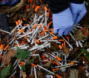 A drug syringe found behind a vacant property in northeast Albuquerque, N.M., is placed into a container on Friday, Aug. 9, 2019, as crews attempt to clear the lot of needles and other heroin paraphernalia.