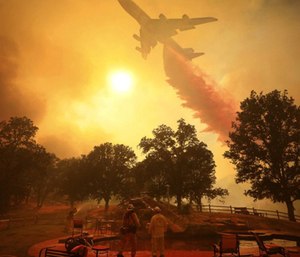 A 747 Global Airtanker makes a drop in front of advancing flames from a wildfire.
