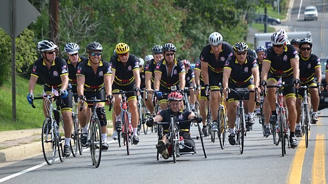 The cyclist leading the group is Evan Marcy, a veteran who sustained a serious leg injury yet rode the entire route with the group in previous years' rides.