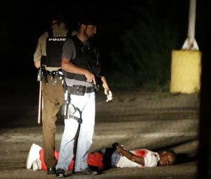 Police stand near a suspect in a parking lot after gunfire during a protest on the anniversary of the death of Michael Brown, Sunday, Aug. 9, 2015. (AP Image)