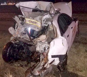 March 20, 2019 photo provided by the Illinois State Police, the squad car of a trooper is crushed after a semi-trailer struck an Illinois State Police trooper and his squad car while he was responding to a multi-vehicle accident. (Illinois State Police via AP)