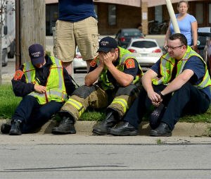 A firefighter puts his head in his hands as he and other firefighters sit on the curb. Dennis Rodeman, a 35-year-old Lansing firefighter has died after being struck by a hit-and-run driver as he collected money for charity.