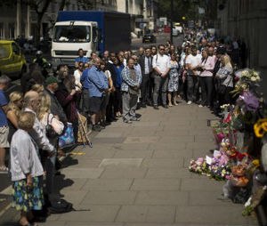 People stand together just before the start of a nationwide minute's silence on the 10 year anniversary of the 7/7 London attacks which killed 52 people, facing in the direction of a plaque and flowers laid at the location of where a suicide bomber blew themselves up during the morning rush hour on a bus in Tavistock Square, London, Tuesday, July 7, 2015. (AP Photo/Matt Dunham)