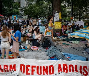 Protesters rest on a grassy area surrounded by signs calling for the changes and abolition of police forces at an encampment outside City Hall in New York.