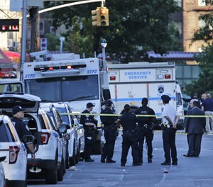 Emergency personnel stand near the scene where a police officer was fatally shot while sitting in a marked vehicle in the Bronx section of New York, Wednesday, July 5, 2017. Police said Officer Miosotis Familia died at a hospital early Wednesday.
