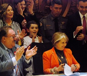 Democratic New Mexico Gov. Michelle Lujan Grisham, sitting right, signs a bill into law that expands background checks to nearly all gun sales in New Mexico in a ceremony in in Santa Fe, N.M. (AP Photo/Morgan Lee)