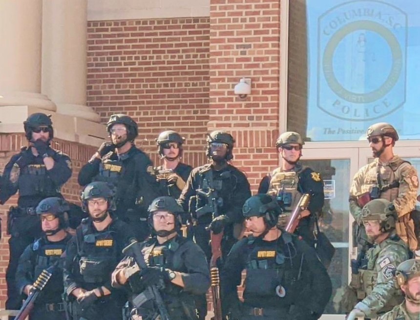 A joint team of SRT operators (black uniforms) and SLED agents (camouflage uniforms) defend the entrance to Columbia Police Department headquarters during the rioting of May 30-31, 2020.