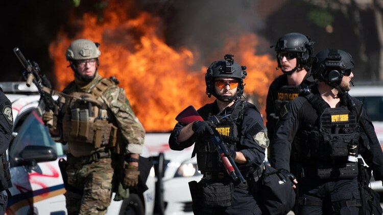 A SLED agent in camouflage and RCSD’s Special Response Team operators in black are seen fanning out on the streets of Columbia, S.C. as a CPD vehicle burns behind them during the riots of May 30-31, 2020.