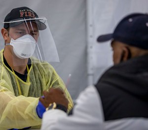 Firefighter Blake Heidrich helps Roderick Bradley self-administer his COVID-19 test at Operation Shelter to Home in the San Diego Convention Center.