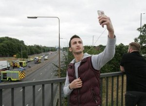Man taking a selfie in front of a motor vehicle collision (Photo Twitter @DailyMirror)