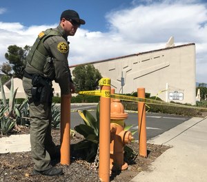 A sheriff's deputy ties crime scene tape in front of Geneva Presbyterian Church on Sunday, May 15, 2022, in Laguna Woods, CA. One person was killed and four others were critically wounded Sunday during a shooting at a church in Laguna Woods.