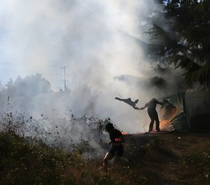 Residents of a tent encampent try and put out a fire that spread to the brush.