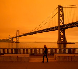 A woman walks under a smoke-filled sky in San Francisco, Calif. on Sept. 9, 2020. A recent study shows wildfire smoke may carry trillions of microbes that can cause illness in firefighters and residents.