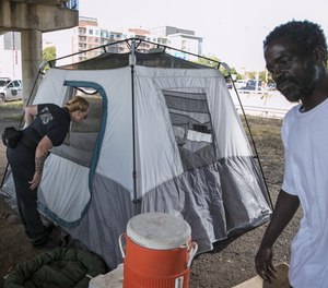 Amber Price, a community health paramedic and founding member of the city's Homeless Outreach Street Team, checks on a homeless woman in a tent under Interstate 35 at Cesar Chavez Street. At right is Doug Huddleston, who also lives under the overpass. (Photo/Tribune News Service by Jay Janner, American-Statesman)