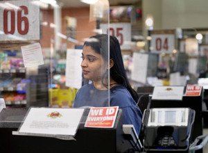 Rehanna Hussain, front-end store manager, is shielded by a protective barrier at the checkout register at Dave's Markets grocery store in Ohio City on Thursday, April 2, 2020. Image: Lisa DeJong/The Plain Dealer