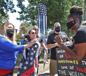 Protester Anne Pungitore (left) talks with counter-protester Tru Edwards at a demonstration outside Hingham Town Hall on Tuesday. More than 100 people, including several firefighters, gathered to protest the town's order for firefighters to remove the 