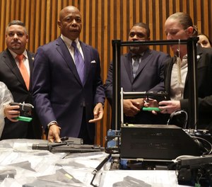 Mayor Eric Adams, middle, flanked by NYPD Commissioner Edward Caban, left, Manhattan DA Alvin Bragg and prosecutors, looks at ghost guns and printers during a news conference at NYPD Headquarters.