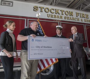 FEMA Administration Fire Grant team member Eve Birge, left, and FEMA Region 9 administrator Bob Fenton present Stockton Fire Chief Richard Edwards, center, and Stockton City Manager Harry E. Black with a ceremonial check during Thursday’s news conference.