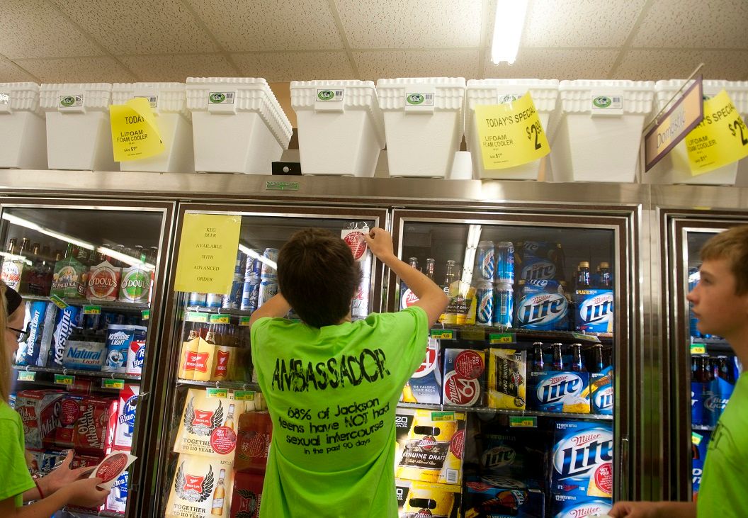 A teen puts a sticker on a beer cooler as part of a project to raise awareness of underage drinking. Image: Sam Gause/MLive Media Group