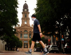 Wearing a mask, Matthew Lubinski of Bedford walks through downtown Fort Worth past the old Tarrant County Courthouse, Thursday, July 2, 2020. As cases of the coronavirus surge to record highs, Gov. Greg Abbott on Thursday ordered Texans to wear face masks in public in counties with outbreaks of COVID-19. Image: Tom Fox/Dallas Morning News via TNS