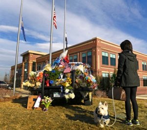 With flags at half staff, Maribeth Forst, with her dog Max, stands near a makeshift memorial on a police cruiser for the victims of what authorities describe as an ambush Monday, Jan. 1, 2018, at the Douglas Country Sheriff Substation in Highlands Ranch, Colo.