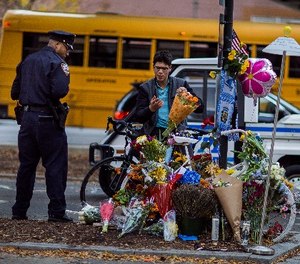A police officer stands guard as Simon Rubin, 25, arranges flowers at a makeshift memorial to remember the victims of the recent truck attack near the crime scene on Thursday, Nov. 2, 2017, in New York.