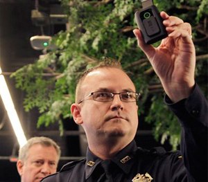 New York Police Department Sgt. Joseph Freer holds a body camera during a news conference while Mayor Bill de Blasio listens.