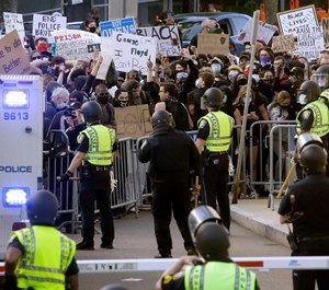 In this May 31, 2020, file photo, protesters, background, demonstrate outside a police station in Boston, over the death of George Floyd who died after being restrained by Minneapolis police officers. (AP Photo/Steven Senne, File)