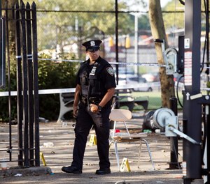 A police officer walks by yellow evidence markers at a playground in the Brownsville neighborhood in the Brooklyn borough of New York, Sunday, July 28, 2019. (AP Photo/Mark Lennihan)