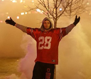 An Ohio State fan stands in a cloud of tear gas as police officers try to disperse a crowd of Ohio State fans trying to block High Street in Columbus, Ohio, Monday, Jan. 12, 2015. (AP Image)