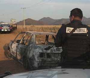 Federal police stand next to a bullet riddled and burned car after a criminal gang ambushed a police convoy near the town of Soyatlan, near Puerto Vallarta, Mexico.