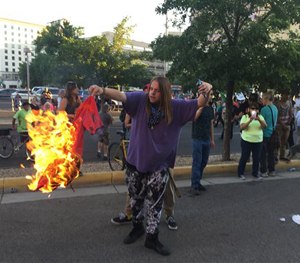 A protestor of Republican presidential candidate Donald Trump holds a burning T-shirt outside a rally for Trump in Albuquerque, Tuesday, May 24, 2016.