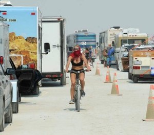 In this Aug. 26, 2013 file photo, a woman rides her bike between cars waiting to enter Burning Man in Gerlach, Nev.