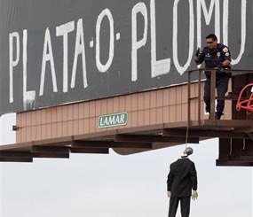 An El Paso, Texas police officer checks a makeshift mannequin Thursday, May 22, 2014, which was left hanging on a billboard along with the message, “silver or lead” in Spanish, a threat heard in Mexico signifying pay up or get shot. El Paso police were investigating two mysterious messages painted onto billboards in the border city that included mannequins dressed in suits hanging from nooses.